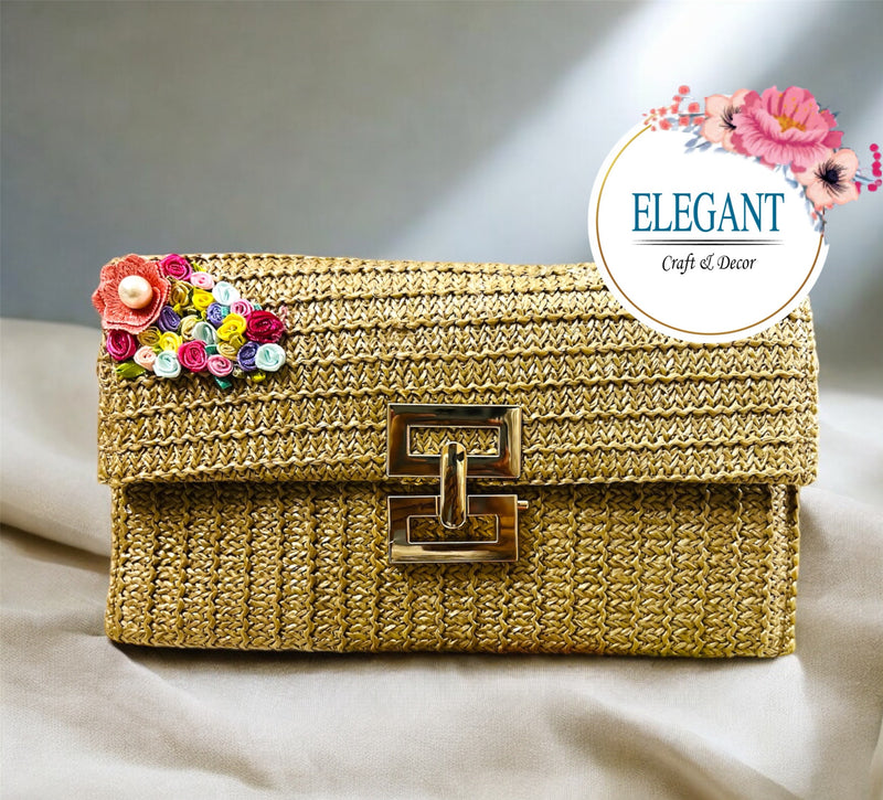 A classy woven clutch in a warm golden tone, featuring a textured finish, elegant metal clasp, and a delicate multicolor floral embellishment for a chic, sophisticated look.