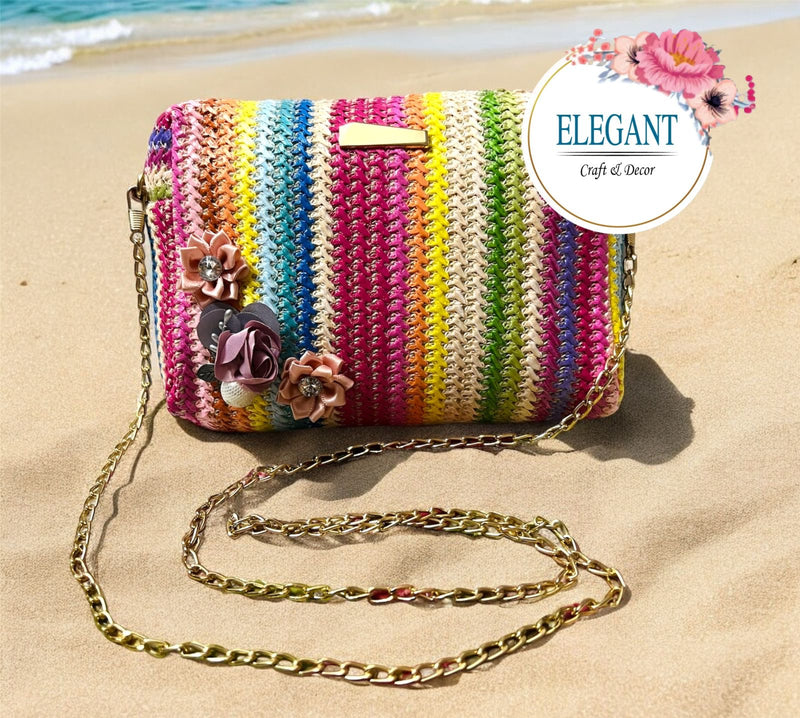 A vibrant handwoven clutch featuring colorful stripes, delicate floral embellishments, and a chic gold chain—perfect for adding a playful yet elegant touch to any outfit.